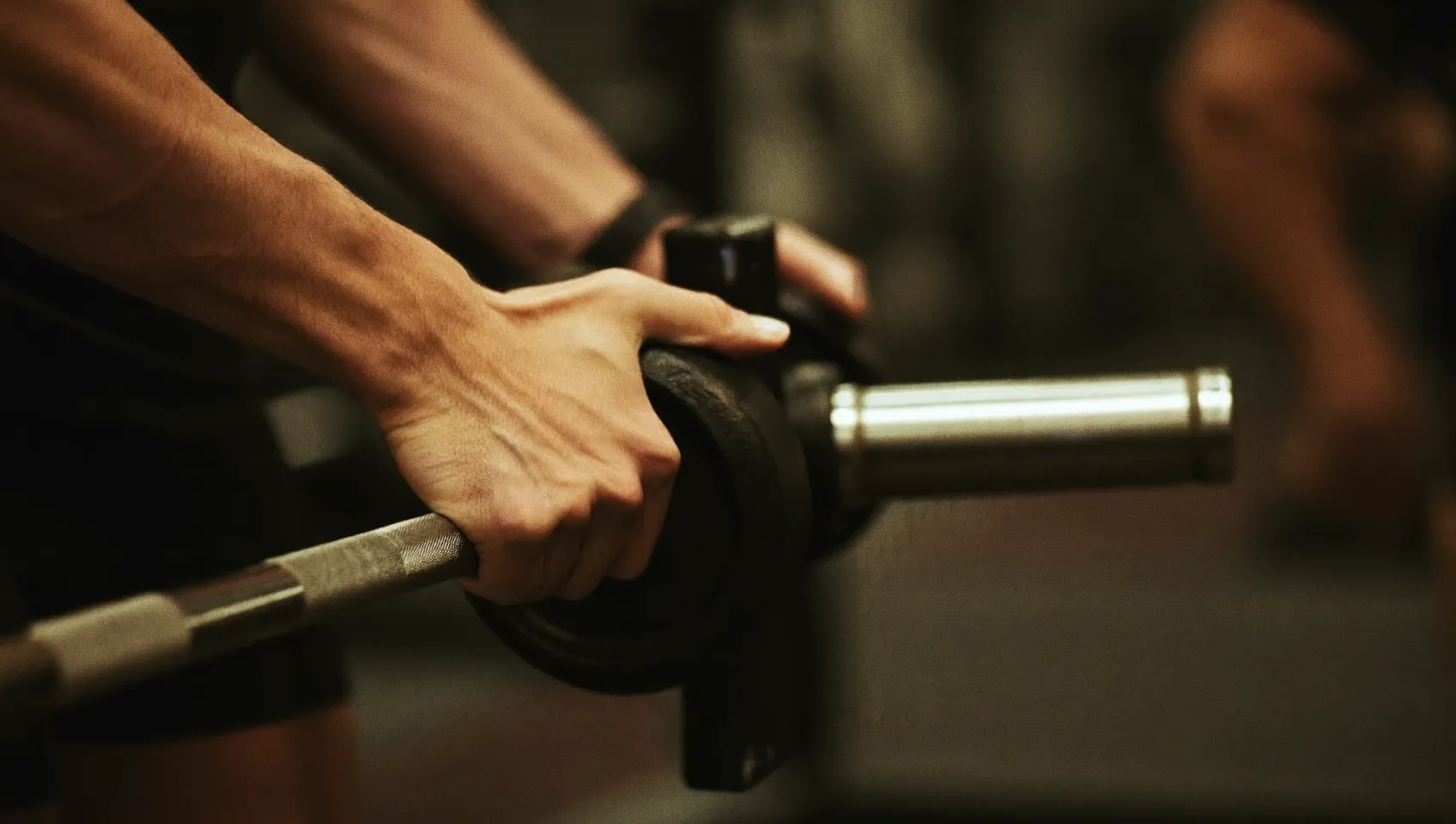 Close-up of hands adding a small weight plate to a barbell to apply progressive overload